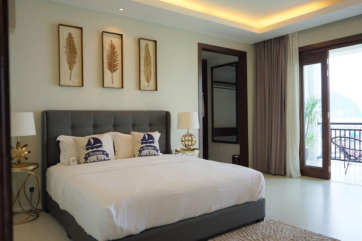 Une chambre d’hôtel moderne dotée d’un grand lit, de deux œuvres d’art accrochées au mur, d’un balcon avec vue et d’un intérieur bien éclairé.