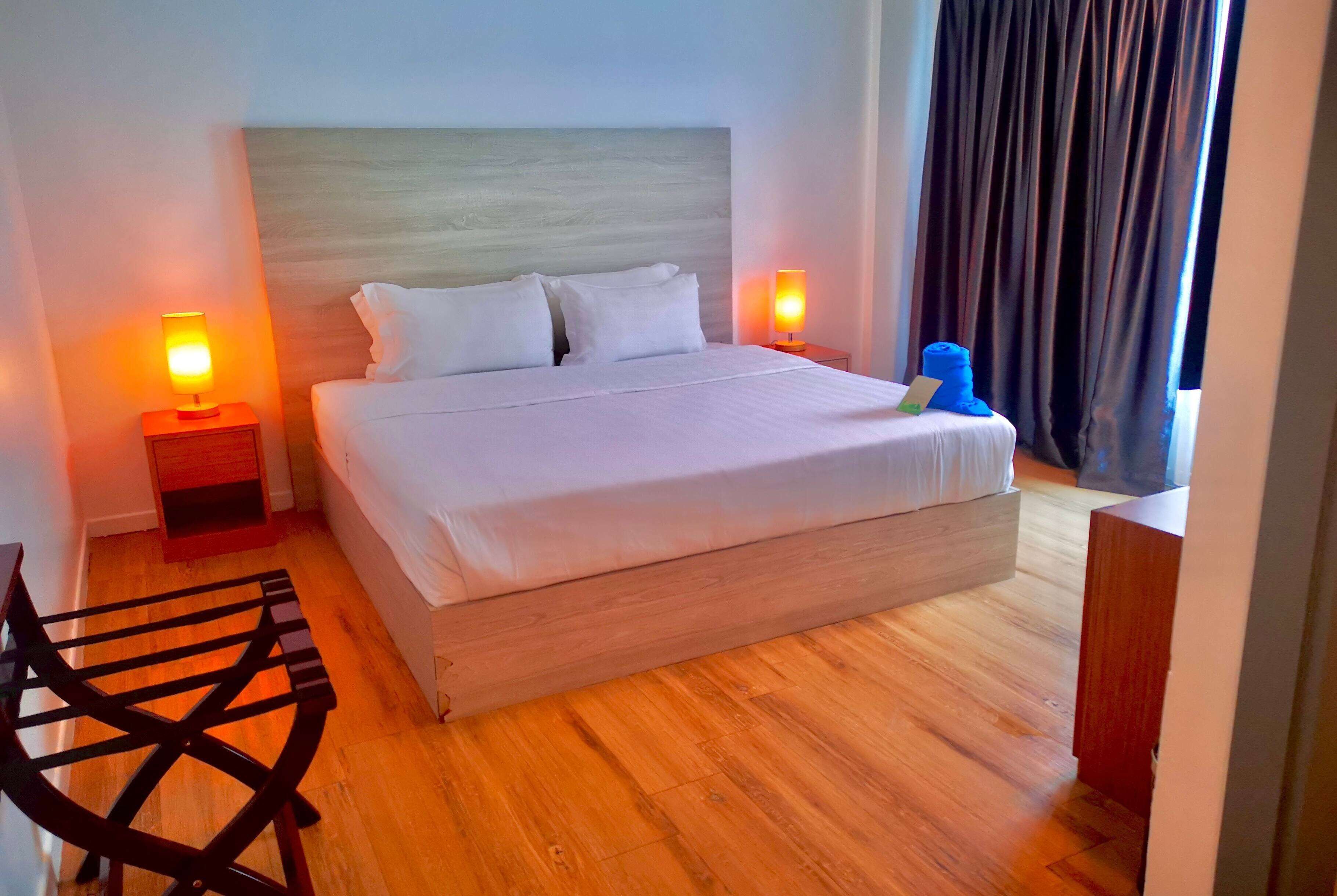 A neatly made bed with white linens, two bedside lamps, a wooden headboard, and a wooden floor.
