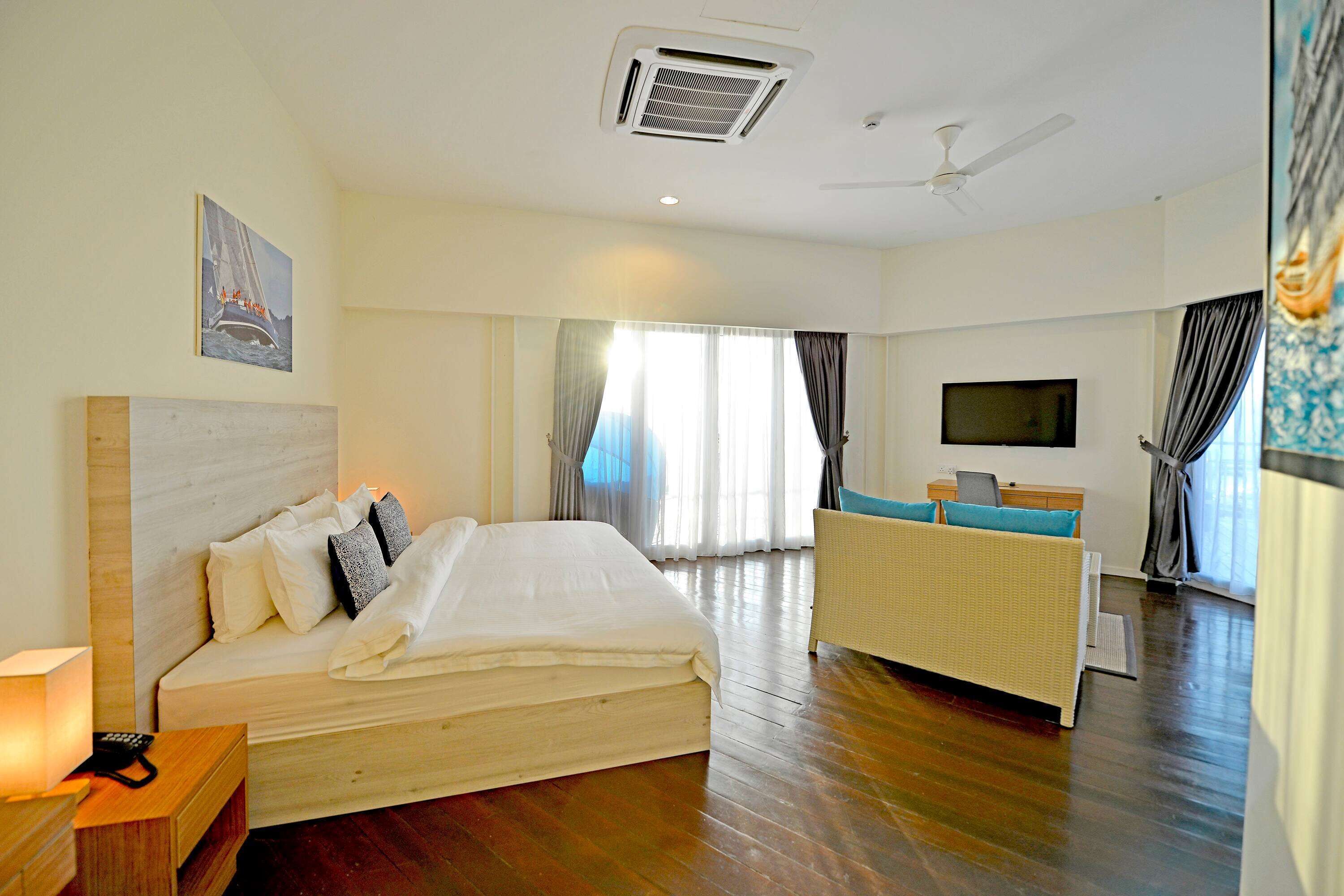 A hotel room with a large bed, a desk with a computer, a TV, and a view of the outdoors through the windows.