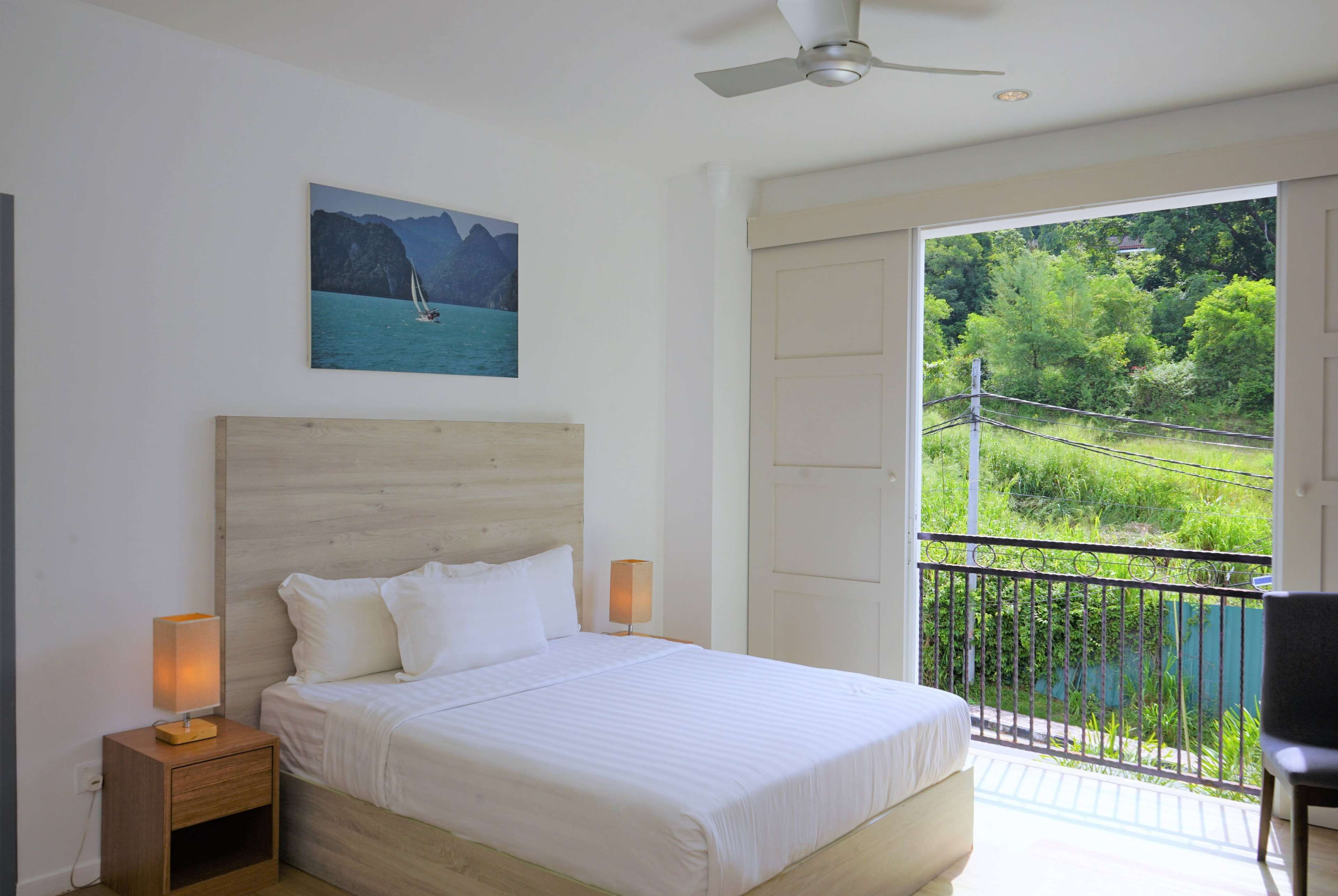 A bedroom with a wooden headboard, a bed with white bedding, two bedside lamps, and a painting of a sailboat on the wall.