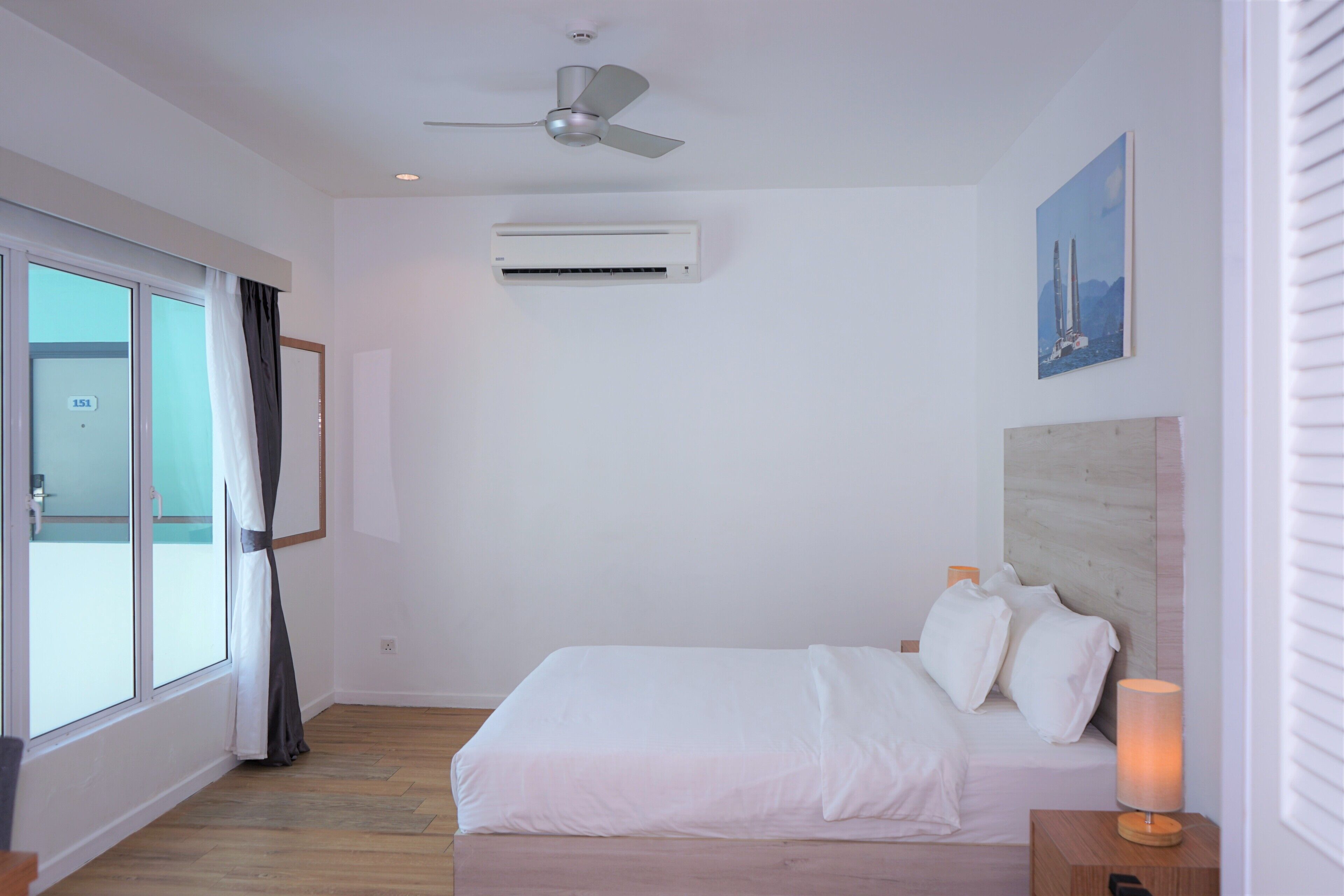 Ein Schlafzimmer mit Bett, Deckenventilator, Klimaanlage, einem Fenster mit Vorhängen und einem Bild an der Wand.
