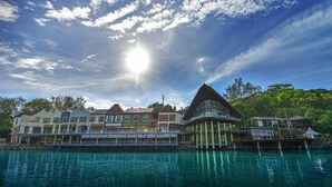 Ein Hotel direkt am Wasser, mit einem markanten Gebäude, das ein großes, dreieckiges Dach und einen überdachten Gang besitzt, der sich über das Wasser erstreckt.