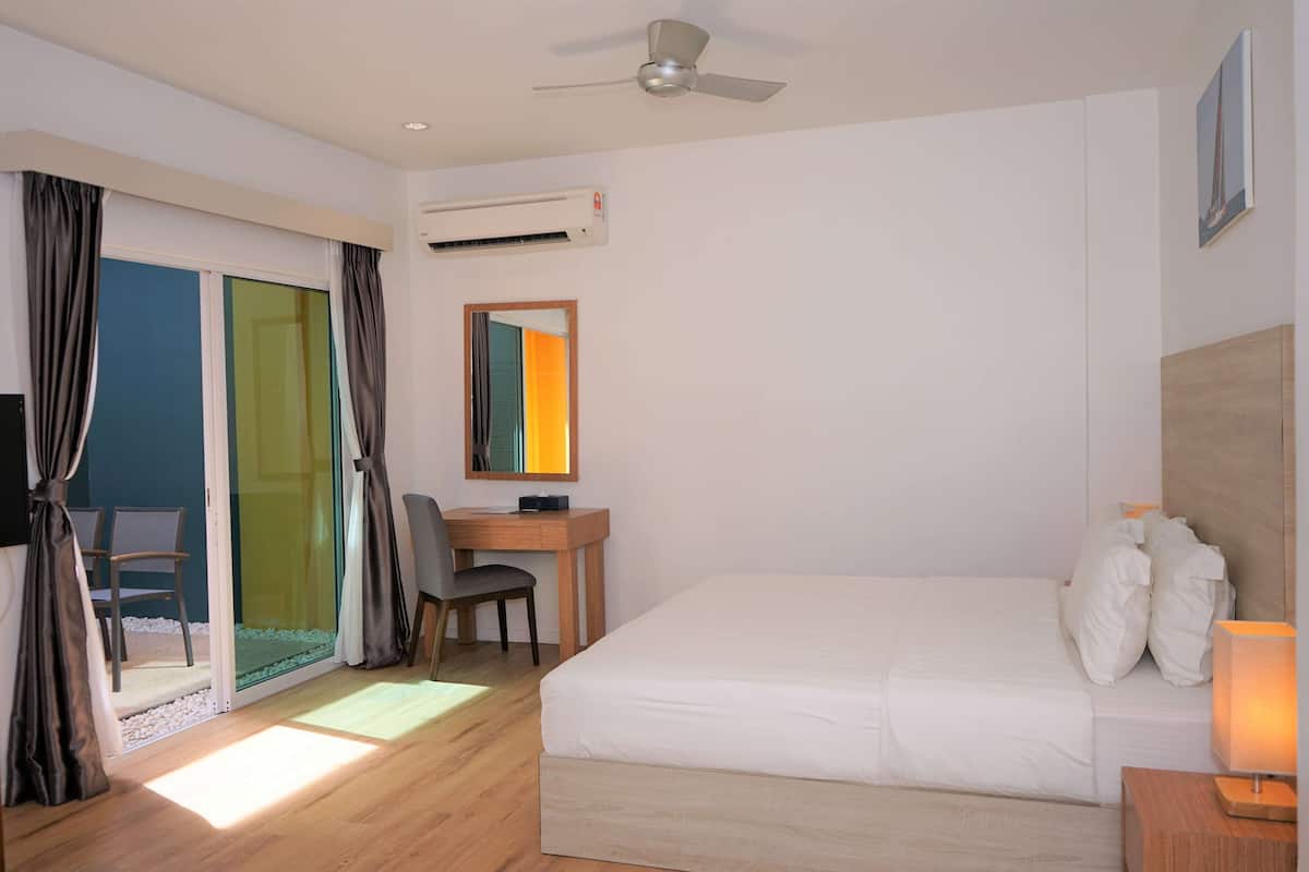 Une chambre d’hôtel équipée d’un lit, d’un bureau, d’une chaise, d’un ventilateur de plafond et d’une porte-fenêtre coulissante.