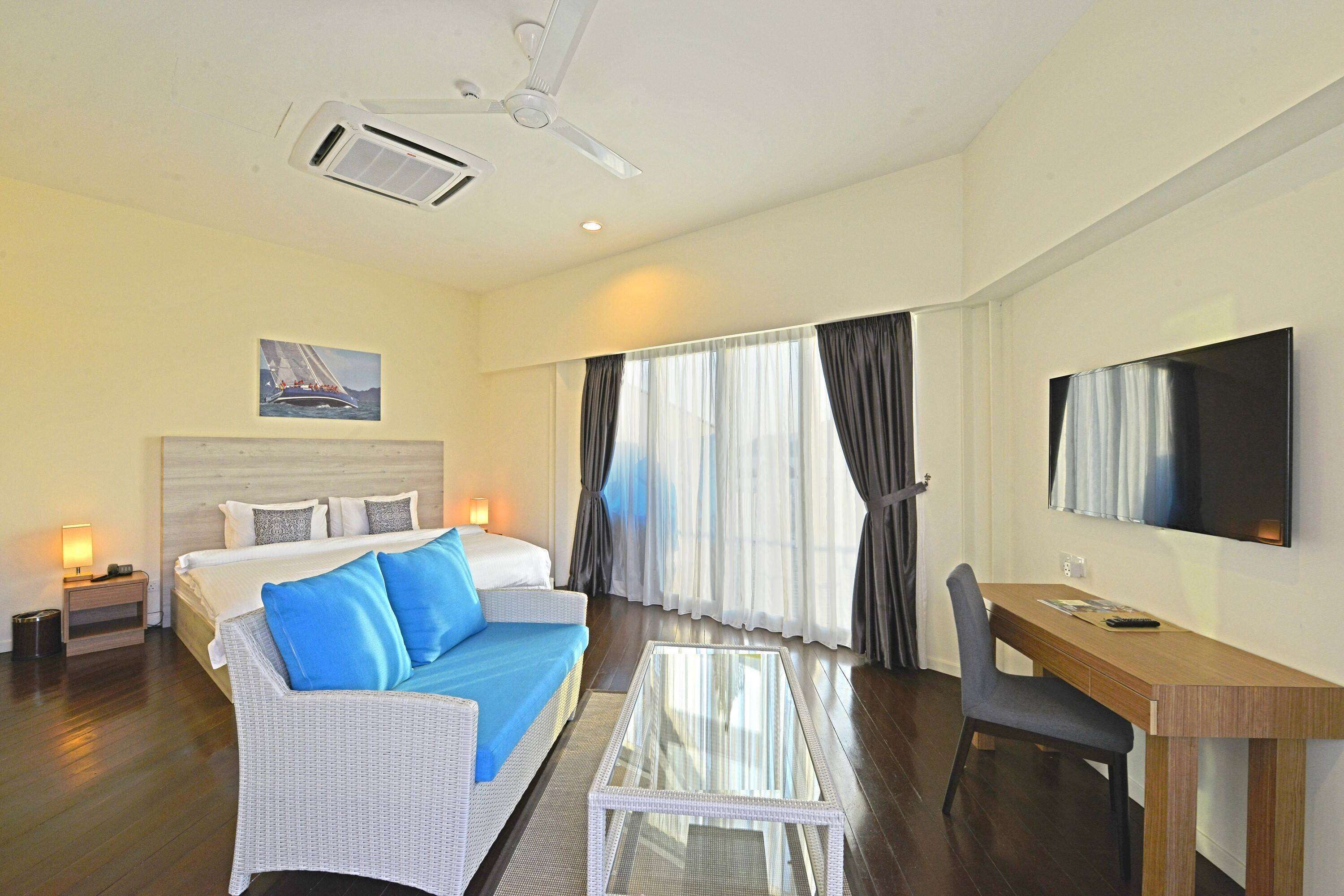 A hotel room with a bed, a sofa, a desk, a chair, a TV, and a window with curtains.