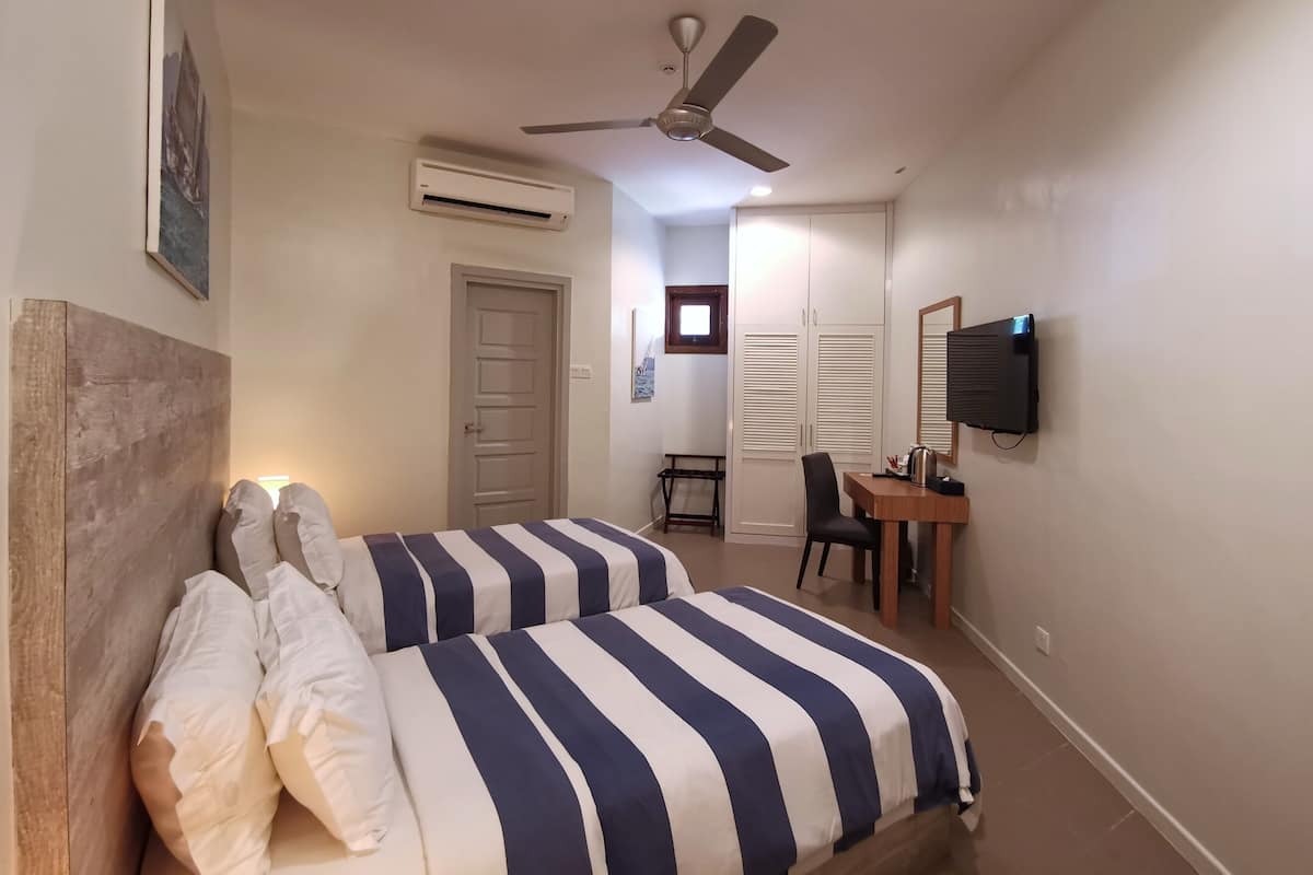 Une chambre avec deux lits, un bureau, une chaise, un ventilateur de plafond, un appareil de climatisation et un téléviseur fixé au mur.