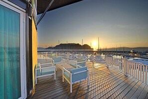 Une terrasse en bois avec des sièges extérieurs et vue sur le port de plaisance.