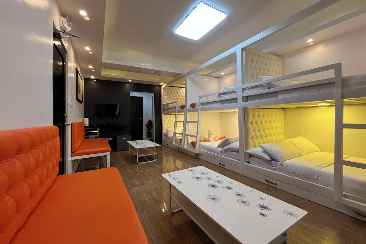 Une chambre d’hôtel compacte avec des lits superposés, un petit coin salon, une table et un téléviseur.