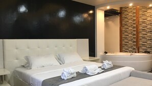 A modern hotel room with a large bed, a separate sofa, a bathtub, and a stone-patterned wall.