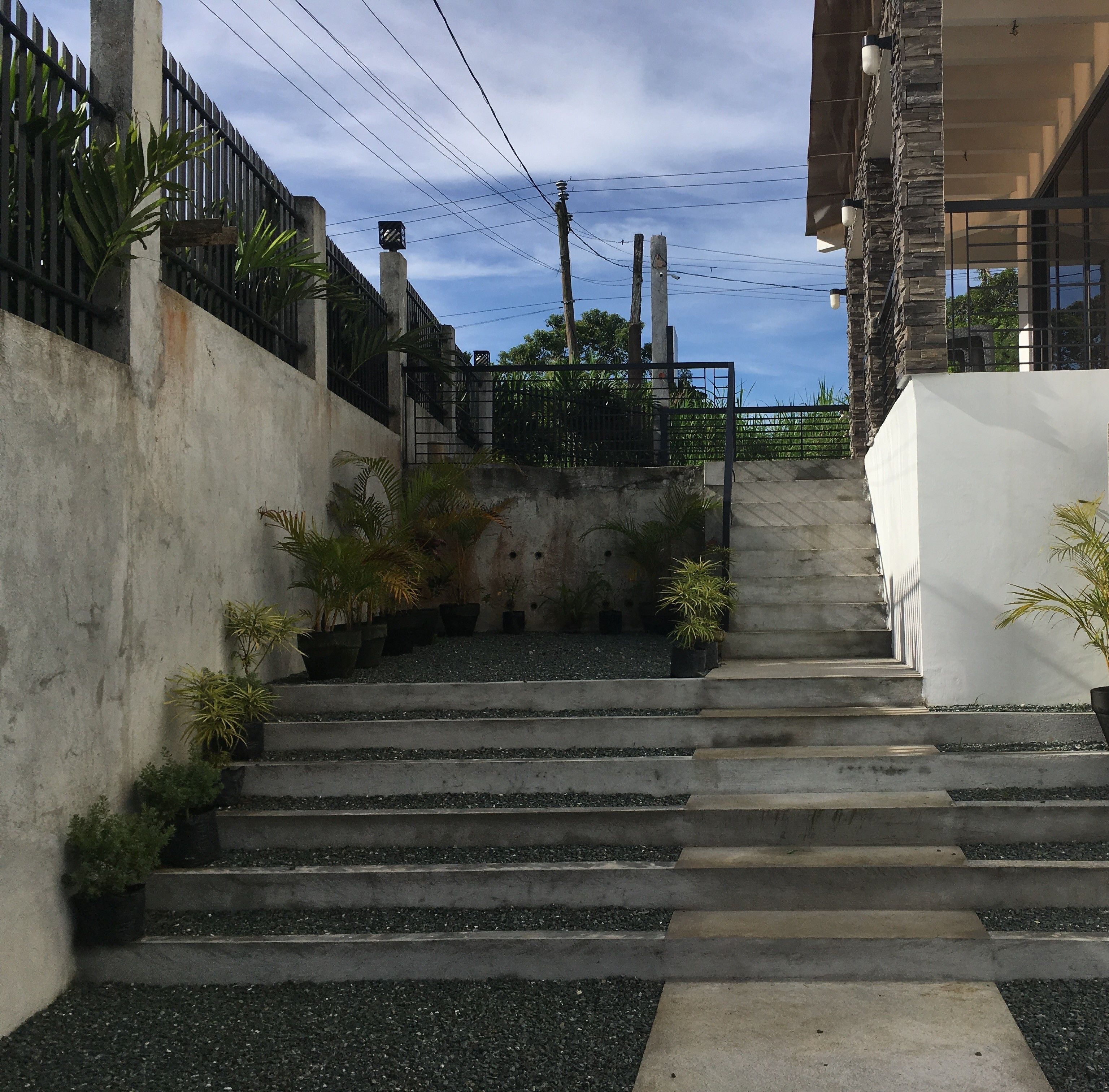 A set of concrete steps leading up to a gated entrance, surrounded by potted plants and a metal fence.