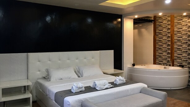 A modern bedroom with a large bed, a sitting area, and a separate bathroom with a bathtub.