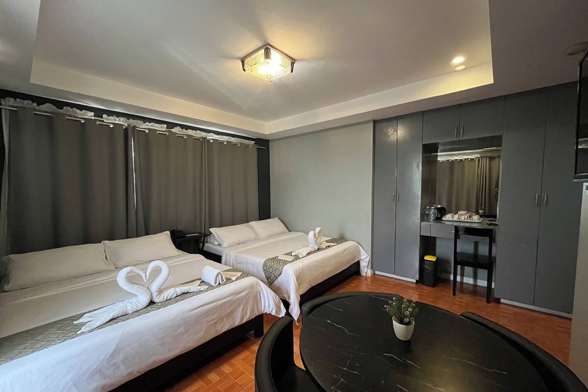 Une chambre d’hôtel avec deux lits, un bureau, une chaise, une petite table et une plante en pot.