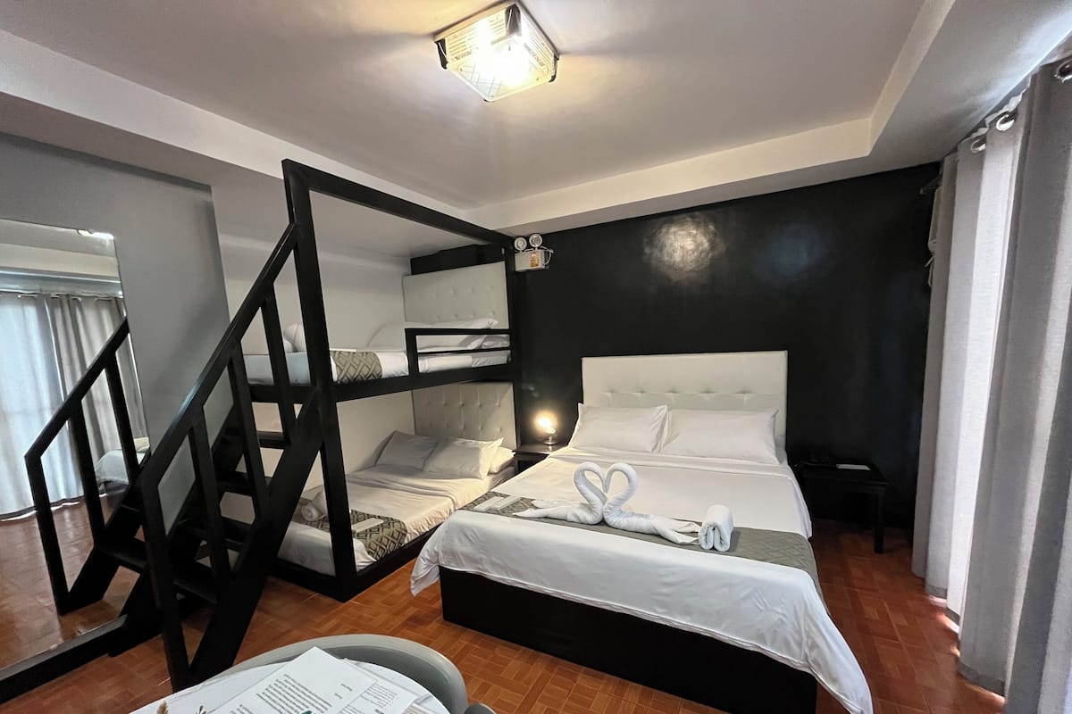 Une chambre avec un lit superposé, un bureau avec une chaise et un lit agrémenté d’une décoration en forme de cœur faite avec des serviettes.