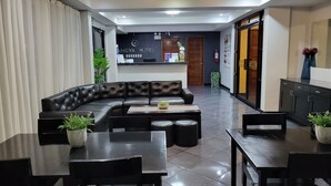 A hotel lobby with a black leather sofa, a reception desk, and a dining area with tables and chairs.