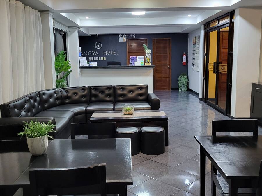A hotel lobby with a black leather sofa, a reception desk, and a dining area with tables and chairs.