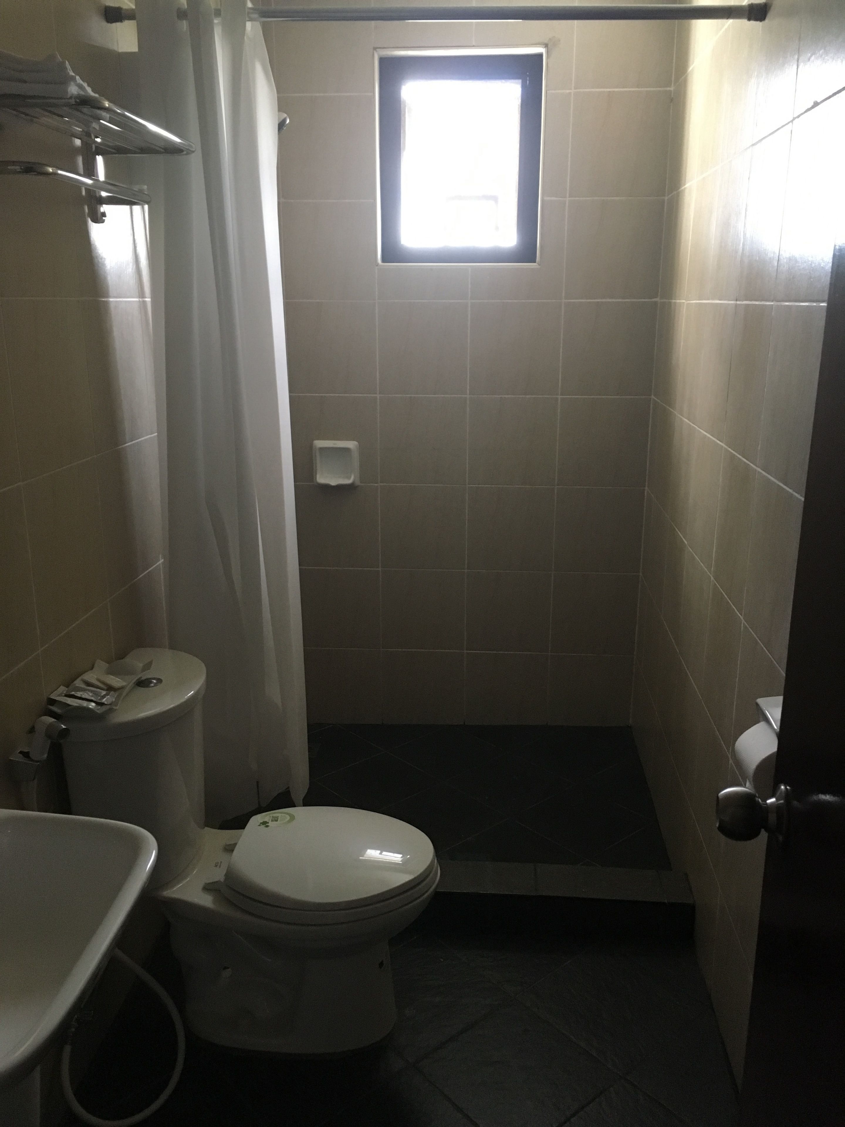 Un baño pequeño y estrecho con inodoro, cabina de ducha y ventana que deja entrar luz natural.
