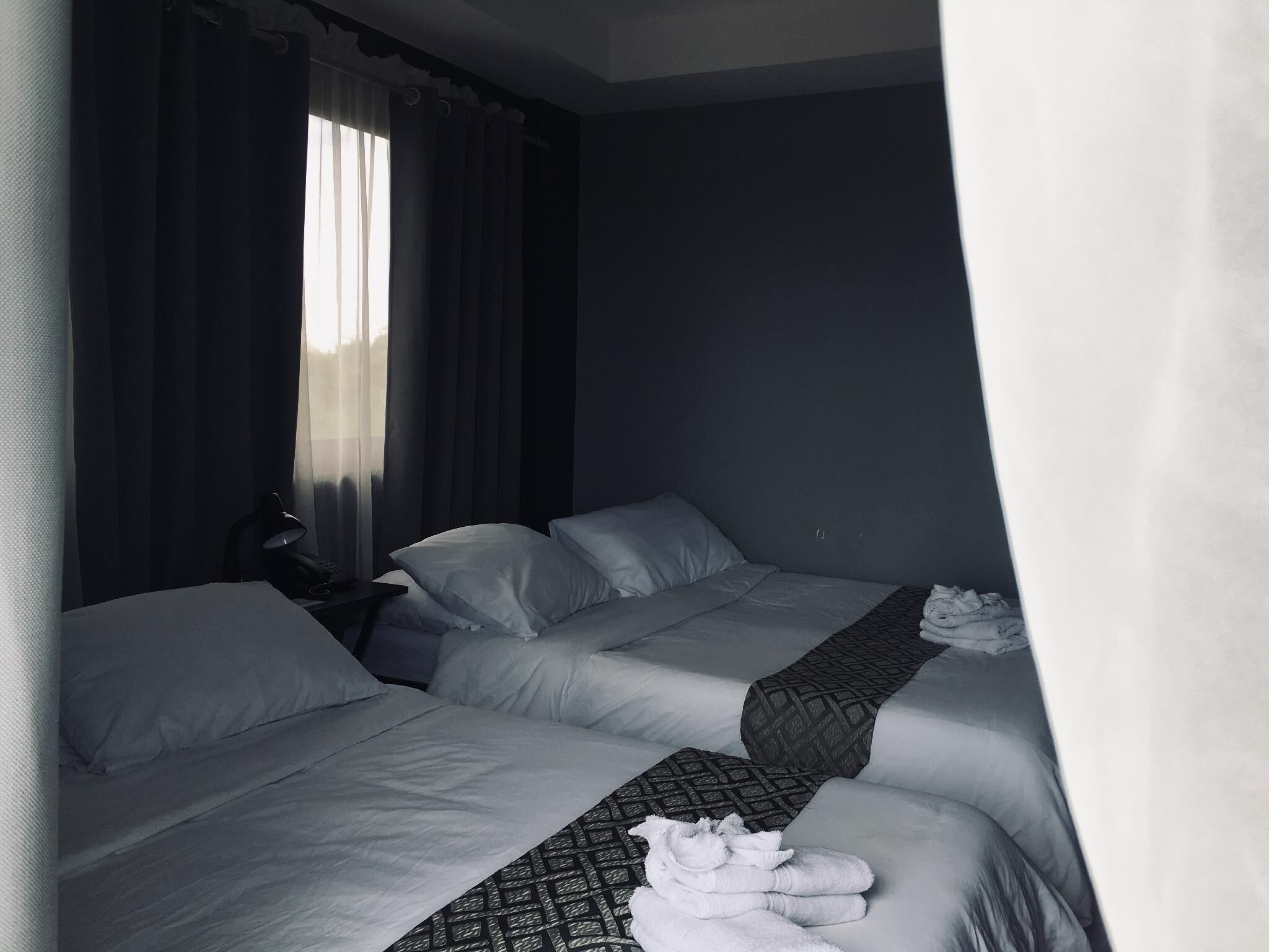 A hotel room with two beds, a desk, and a window with curtains.