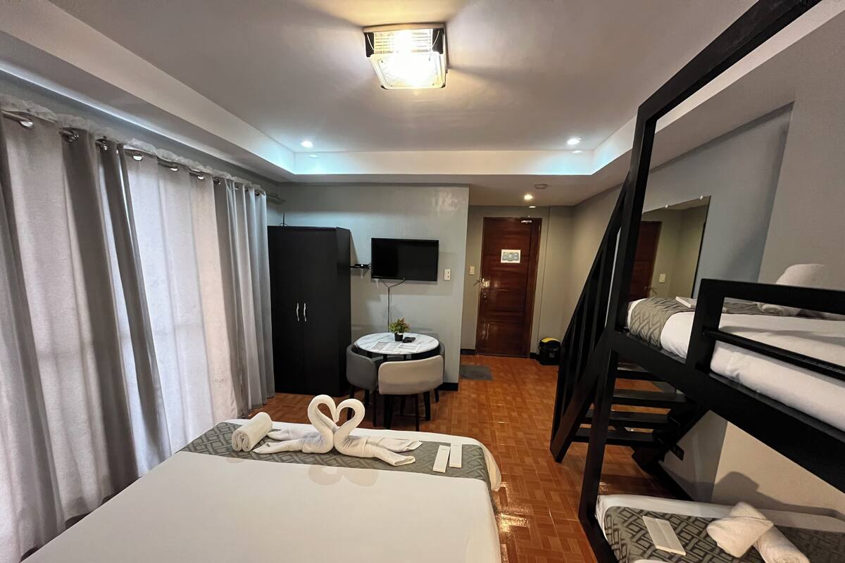 Une chambre d’hôtel équipée d’un lit, d’un bureau, d’une chaise, d’une télévision, d’une armoire et d’un lit superposé.