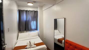 A hotel room with a bed, a small round table, a red sofa, a mirror, and a window with curtains.