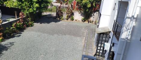 A courtyard with a gravel path, surrounded by lush greenery and a metal gate.