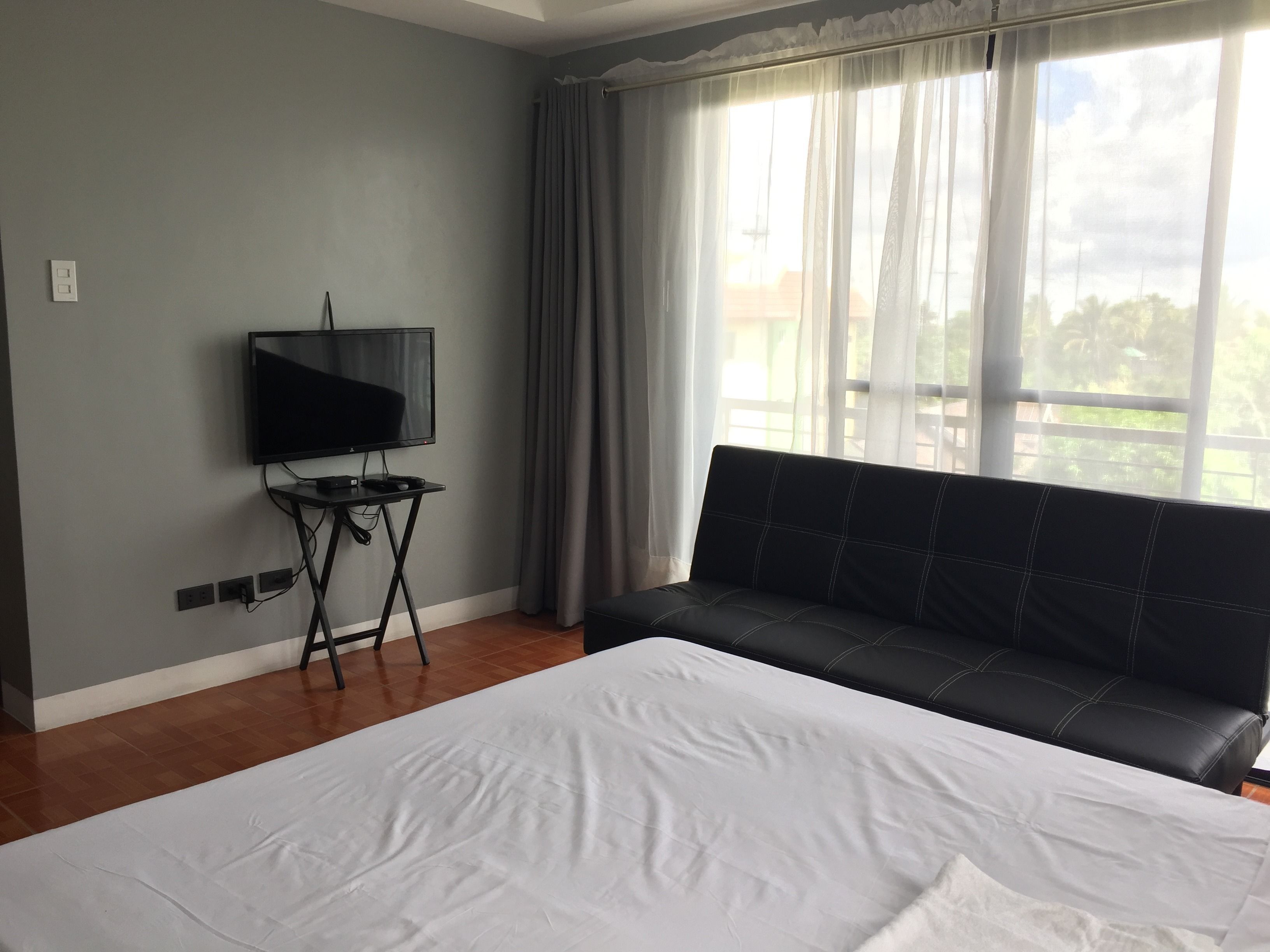 Une chambre d’hôtel avec un grand lit, un téléviseur posé sur une petite table, un canapé et une fenêtre avec des rideaux.