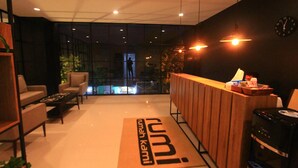 A modern reception area with a wooden desk, a coffee machine, and a view of the cityscape through large windows.