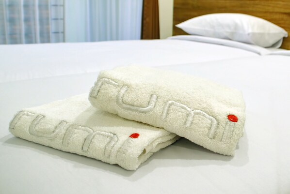 Two neatly folded white towels with embroidered text on a bed. - Rumi Semarang (Semarang)