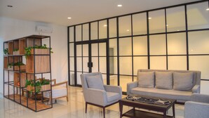 A modern living room with a sofa, armchairs, a coffee table, and a wooden shelving unit with plants.