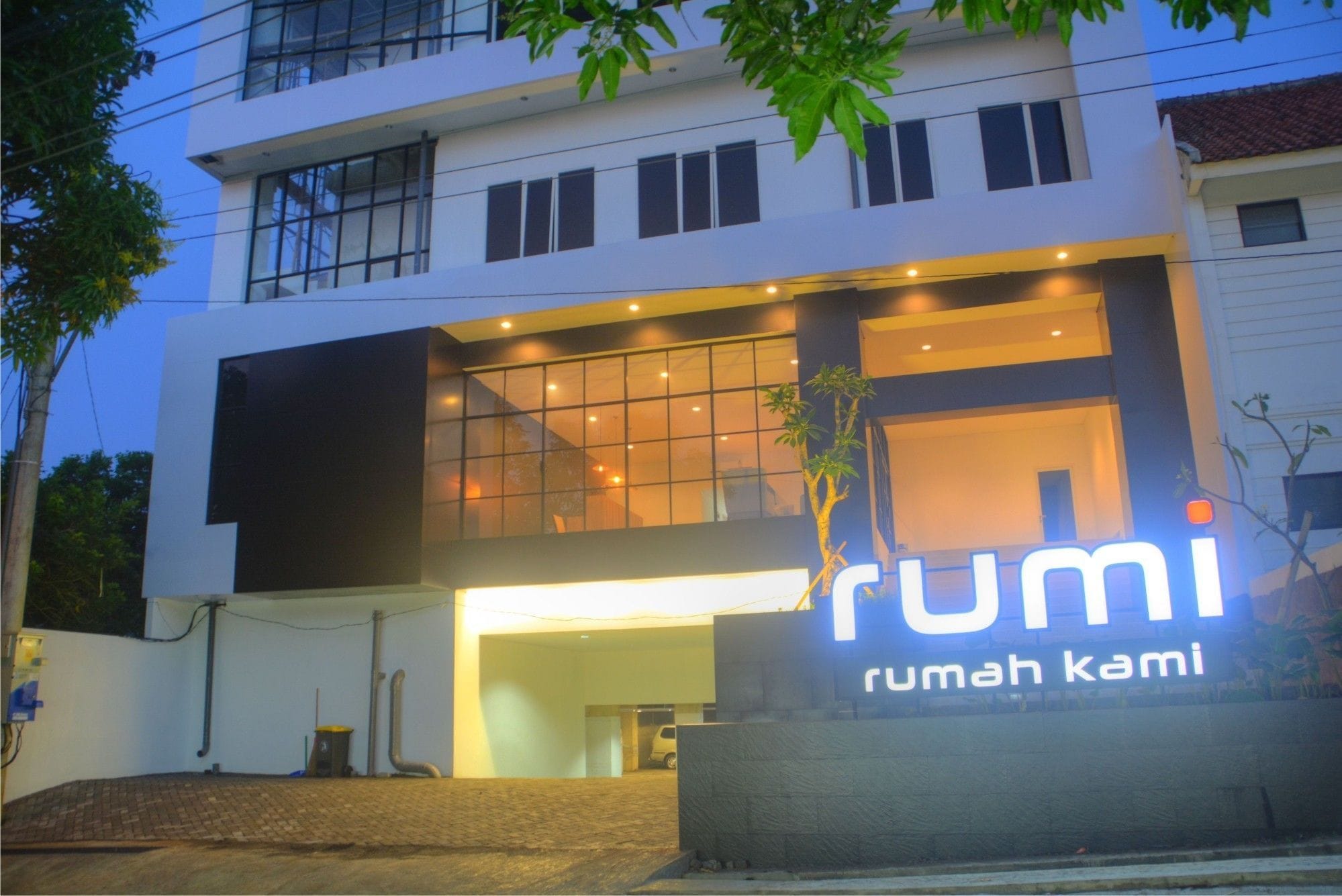 A modern building with a large illuminated sign reading "rumi rumah kami".