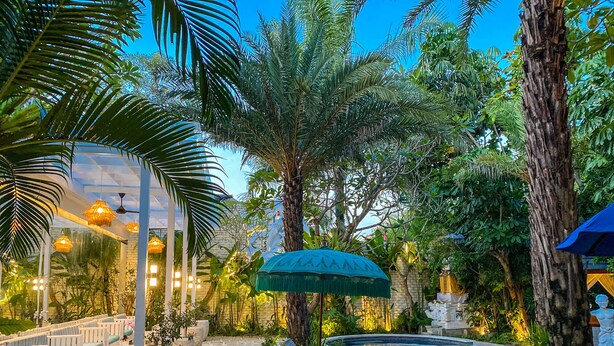 Un espace piscine avec des chaises longues, un parasol bleu et un chemin en pierre.