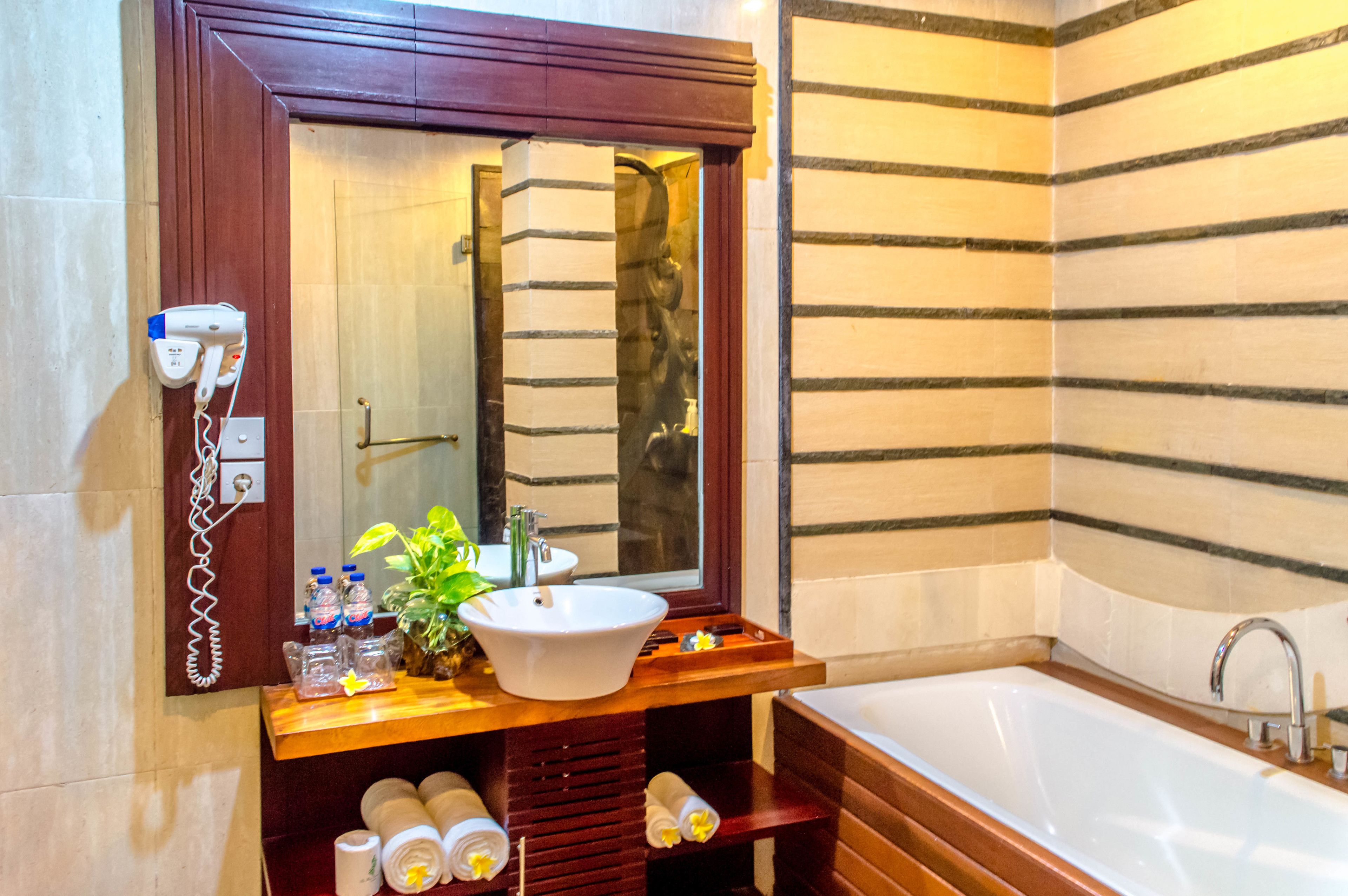 Un baño con tocador de madera, lavamanos blanco, espejo grande y bañera.
