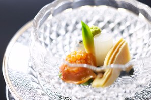 A clear glass bowl with a textured pattern, containing a dessert with a green leaf garnish, a yellow item, and a white item. - Sekizenkan (Nakanojo)