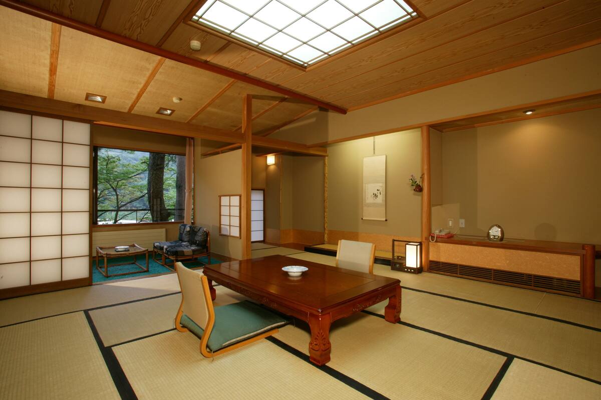Una habitación japonesa tradicional con suelo de tatami, una mesa de madera y un puertas corredera que da a vistas de árboles.