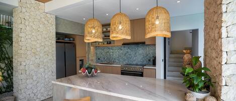 A modern kitchen with a large island, wooden bar stools, and hanging wicker pendant lights.