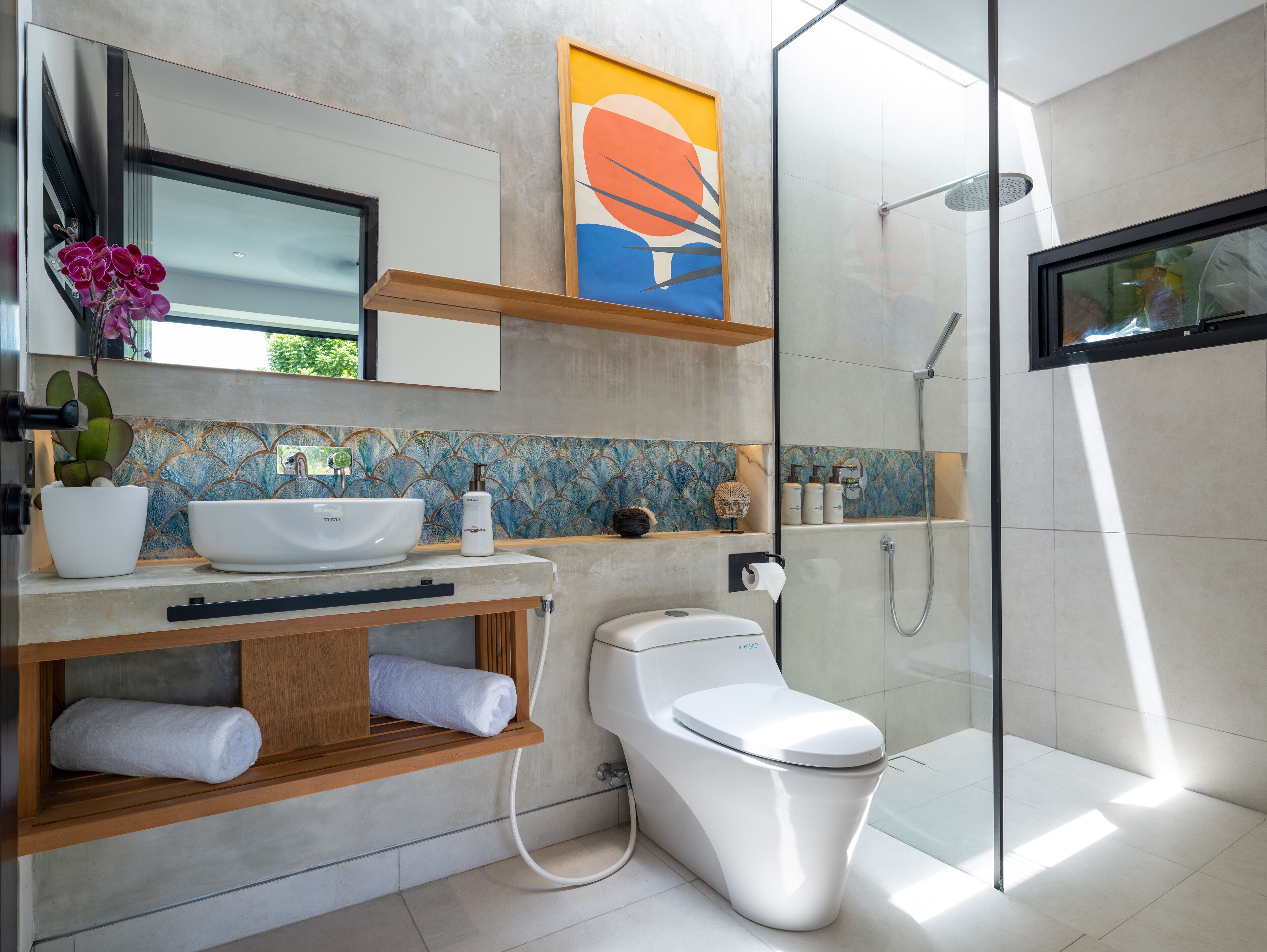 Un baño moderno con cabina de ducha de vidrio, inodoro blanco, lavamanos con un jarrón decorativo y un perchero para toallas.