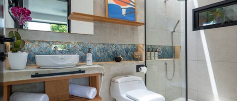 Un baño moderno con cabina de ducha de vidrio, inodoro blanco, lavamanos con un jarrón decorativo y un perchero para toallas.
