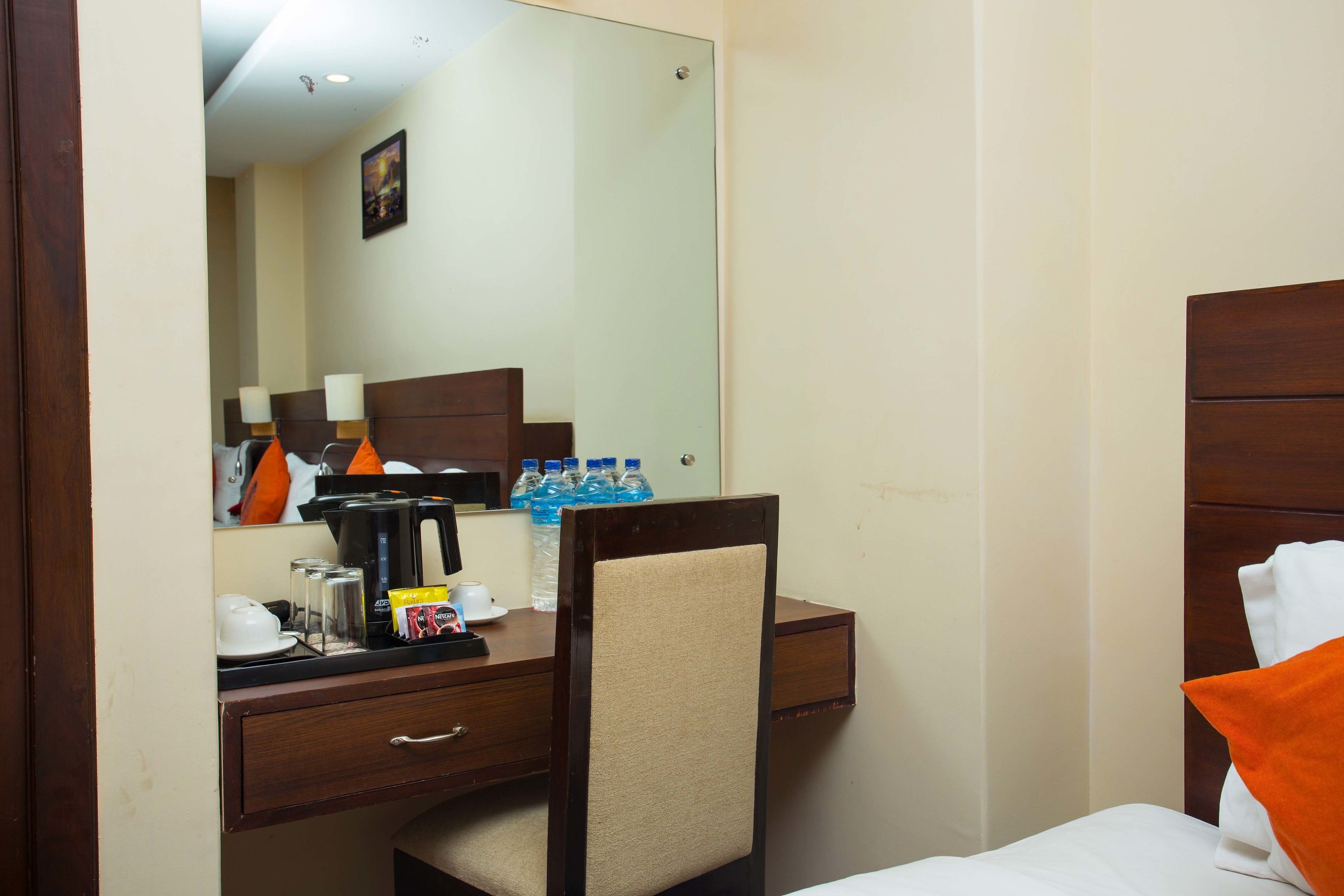 Habitación de hotel con cama, escritorio, silla, espejo y cafetera.
