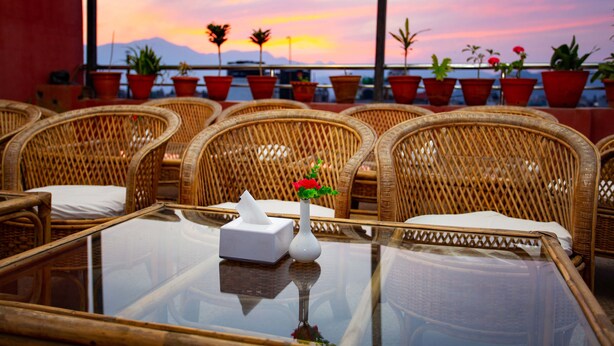 A dining area with wicker chairs and a table, a vase with flowers, and a sunset view through large windows. - Hotel Jay Suites (Kathmandu)