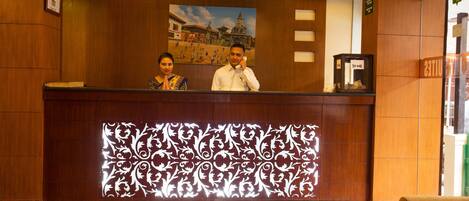 A reception desk with a decorative panel, a framed painting, and a clock.