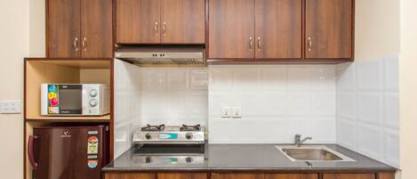 A compact kitchen with wooden cabinets, a microwave, a refrigerator, a stove, and a sink.