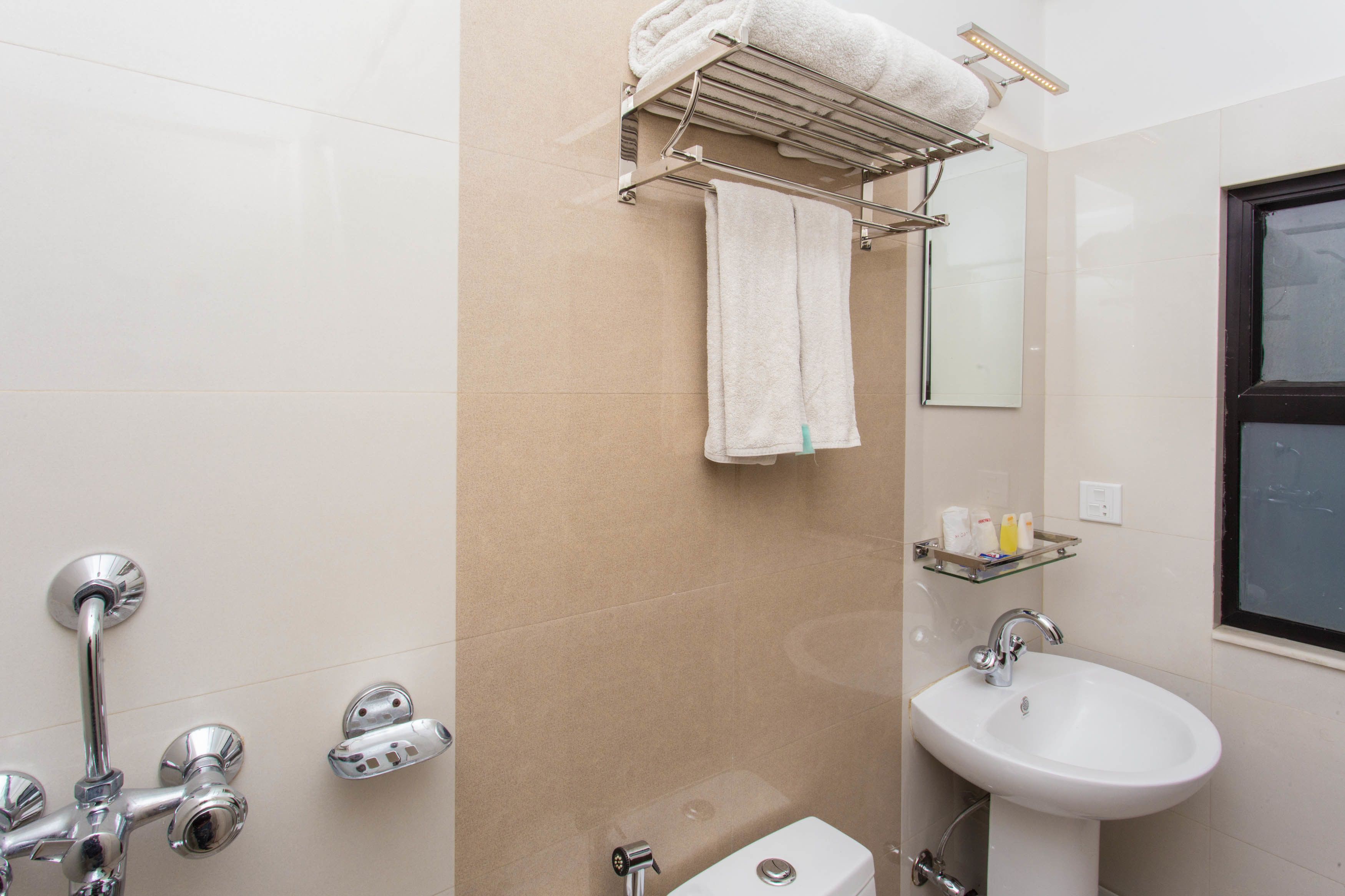 Un baño con lavamanos blanco, repisa de vidrio con artículos de aseo, toallero y ducha con grifería cromada.