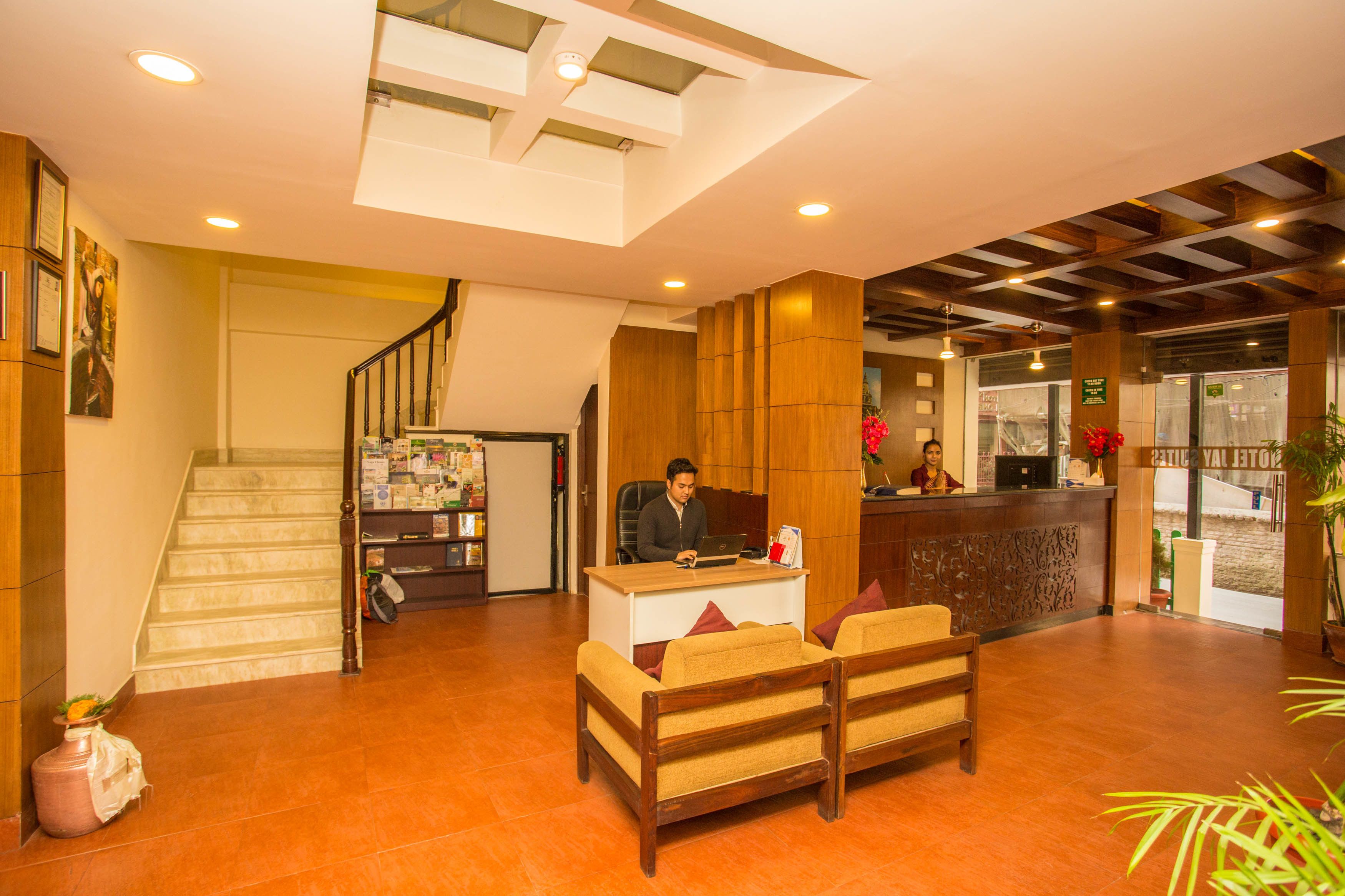 A hotel lobby with a reception desk, a staircase, and a seating area.