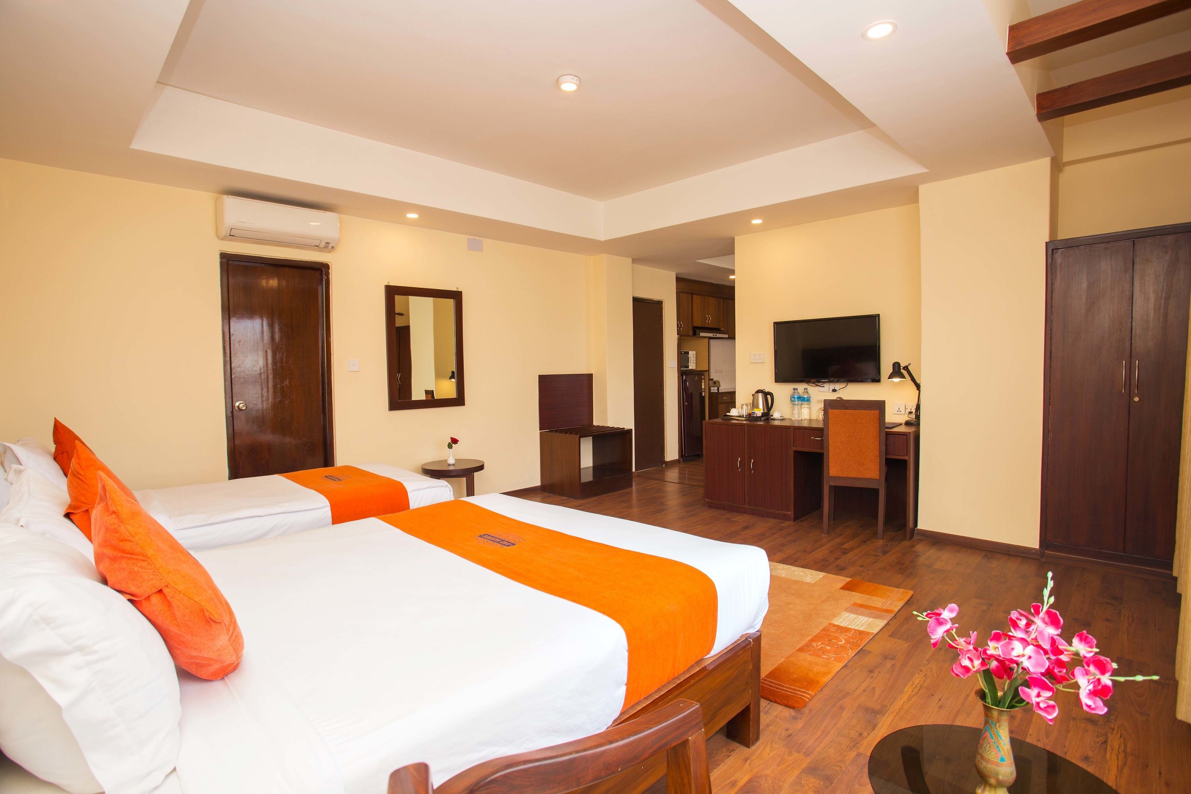 A hotel room with two beds, a desk, a television, and a bathroom visible in the background.