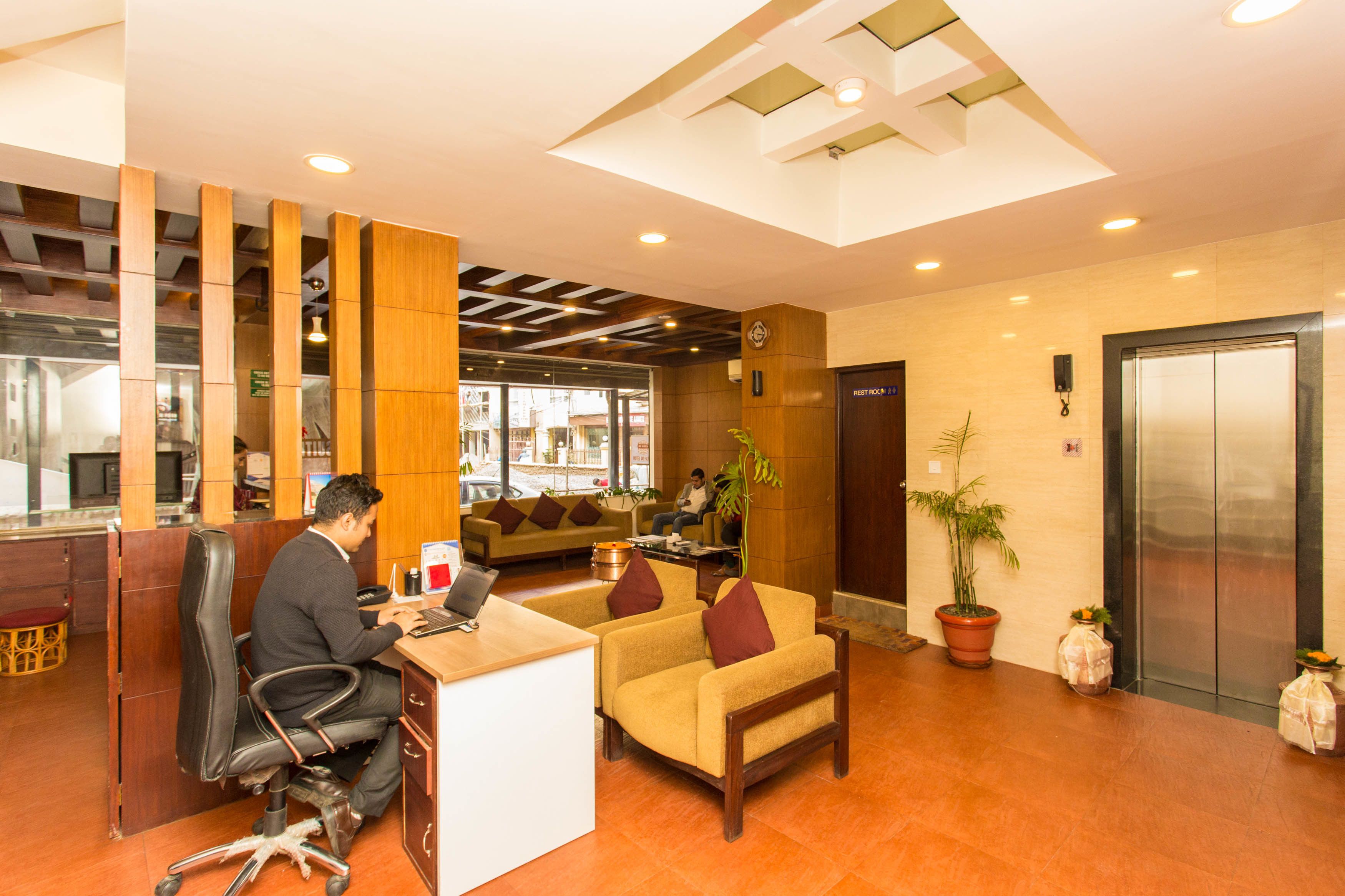 A reception area with a desk, chairs, a sofa, a potted plant, and an elevator.