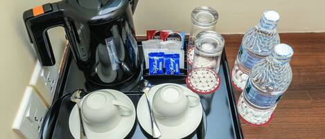 A tray with a coffee maker, two cups, a spoon, a packet of Nescafe, a glass of water, and two bottles of water.