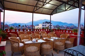 A terrace with wicker furniture and potted plants, overlooking a cityscape with mountains in the background. - Hotel Jay Suites (Kathmandu)