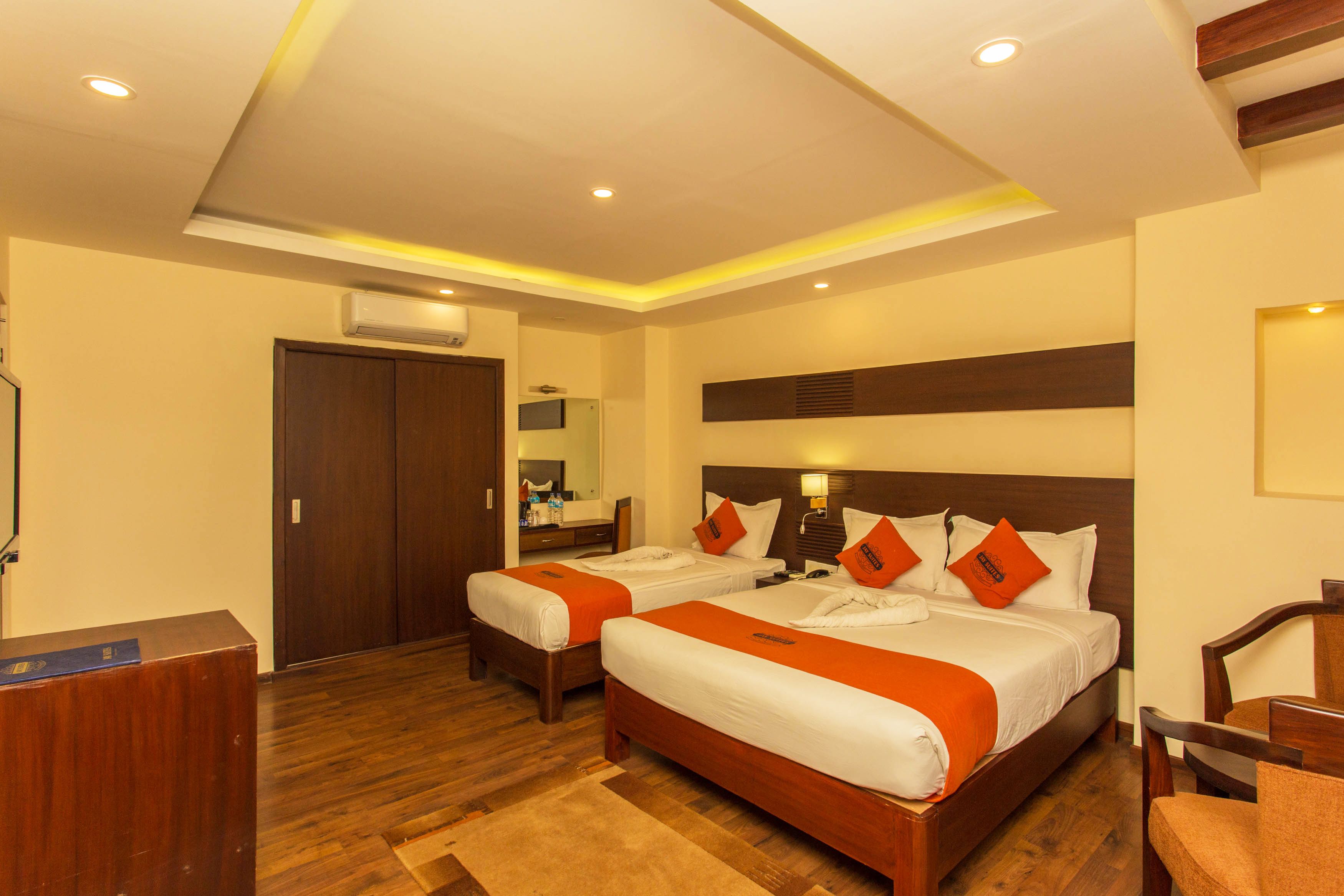 A hotel room with two beds, wooden flooring, a desk, and a chair.