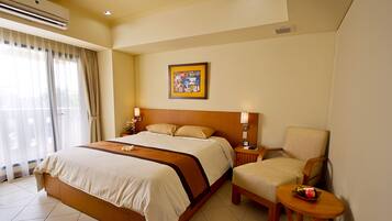 A hotel room with a large bed, a chair, a small table, and a painting on the wall.