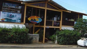 A building with a wooden facade, large windows, and a sign with a wave and mountain design. - Noronha Sol e Mar Pousada (Fernando de Noronha)