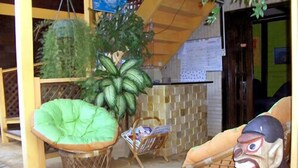 A room with a wooden floor, a green cushioned chair, a wicker chair, a woven basket, and a decorative mask. - Noronha Sol e Mar Pousada (Fernando de Noronha)