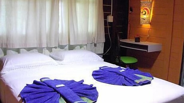 A hotel room with a bed, white curtains, a wall-mounted light, and a small table with a chair. - Noronha Sol e Mar Pousada (Fernando de Noronha)